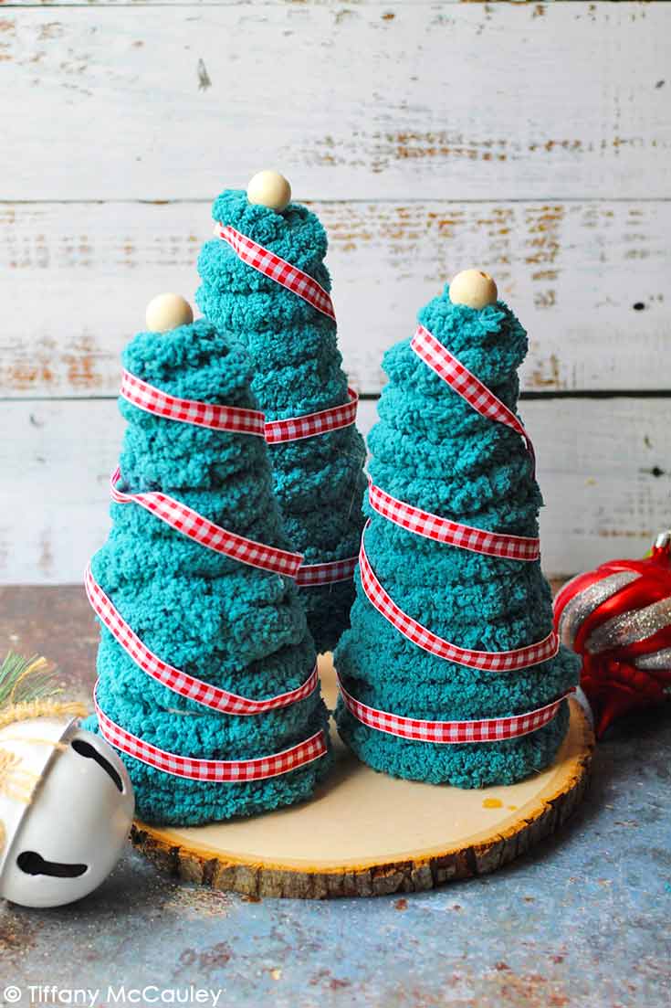 Three Yarn Christmas Trees sit on a wooden base as a beautiful decoration.