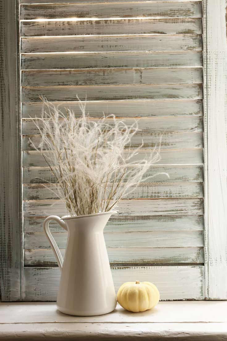 Tips and tricks for How To Get That Farmhouse Look. A pitcher sits in front of a white-washed shutter with a small white pumpkin next to it.