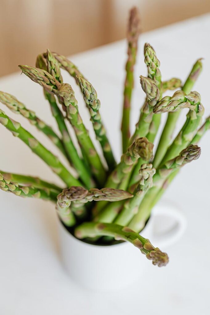 A white mug on a white table holds upright spears of asparagus.