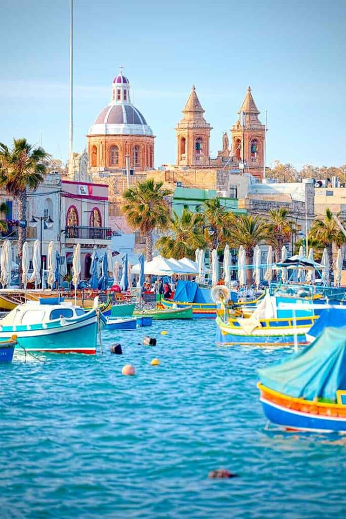 A canal with boats and a Malta town in the background.