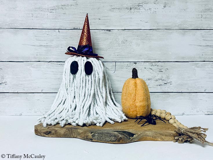 A DIY Halloween ghost made from a mop sits next to a felted pumpkin.