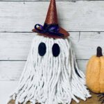A DIY Halloween Ghost on a wood platform next to a felted pumpkin.